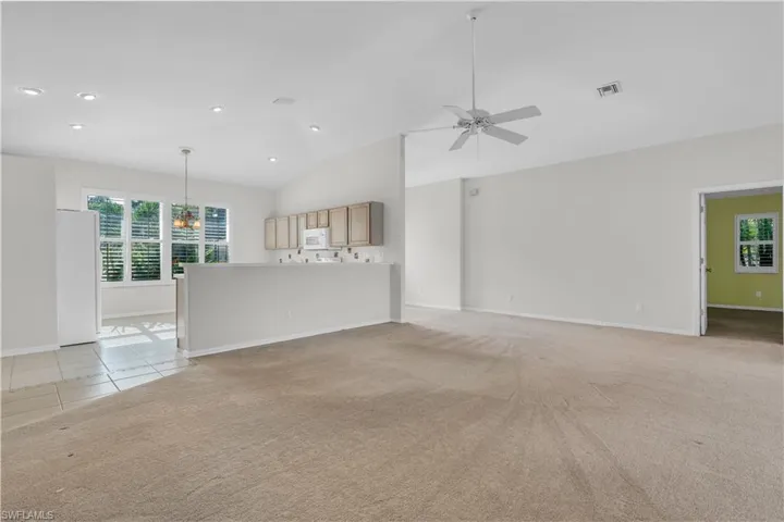 Unfurnished living room featuring light carpet, vaulted ceiling, and ceiling fan with notable chandelier