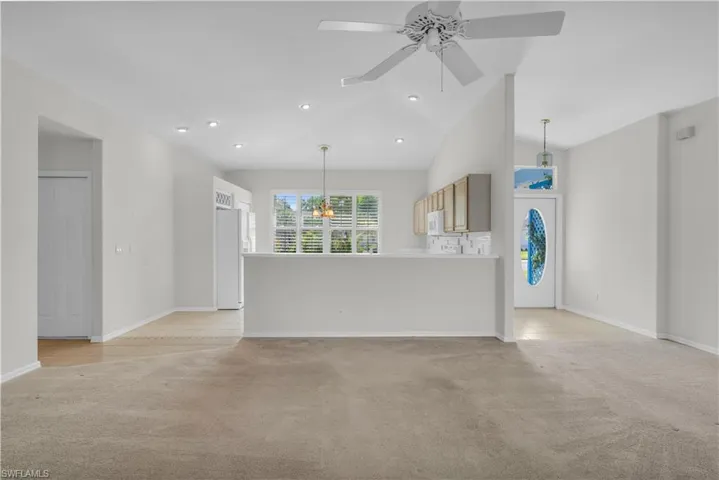 Unfurnished living room featuring ceiling fan with notable chandelier, high vaulted ceiling, and light colored carpet