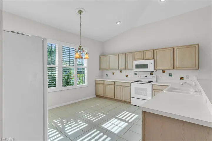 Kitchen featuring sink, light brown cabinets, lofted ceiling, light tile patterned floors, and white appliances