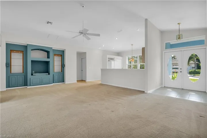 Unfurnished living room featuring built in features, ceiling fan, light colored carpet, high vaulted ceiling, and french doors