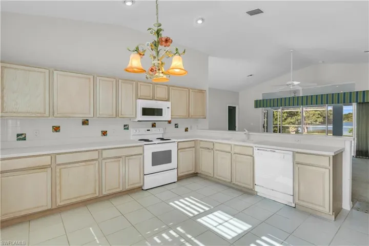 Kitchen with pendant lighting, light brown cabinetry, ceiling fan with notable chandelier, light tile patterned flooring, and white appliances
