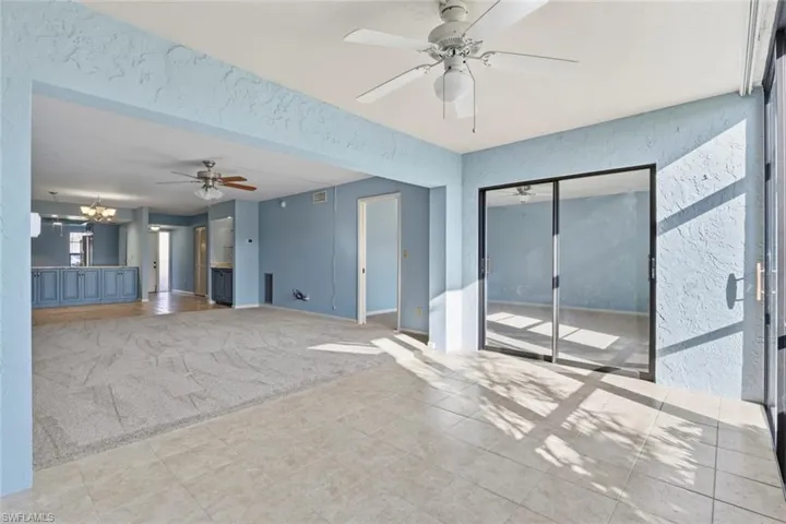 Unfurnished living room featuring light carpet, ceiling fan, a textured wall, and hanging lights