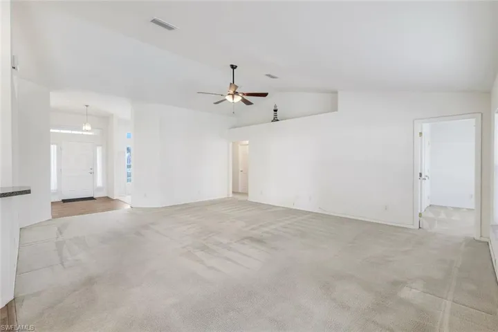 Unfurnished living room featuring ceiling fan, light carpet, and lofted ceiling