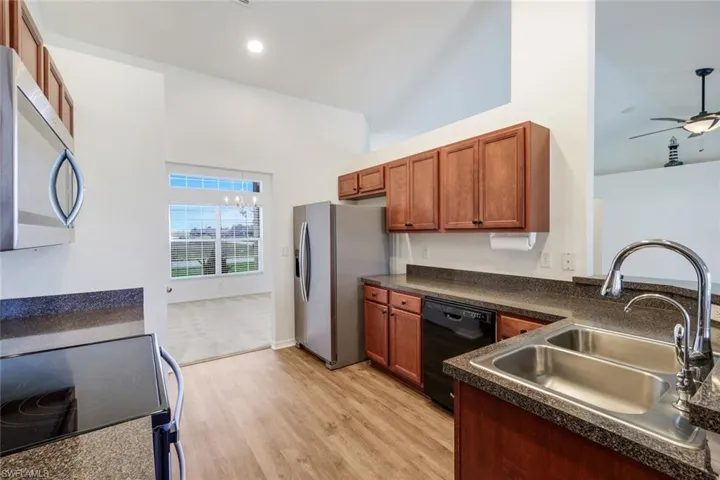 Kitchen featuring dark countertops, stainless steel appliances, wood finish cabinetry, ceiling fan, and light wood-style floors