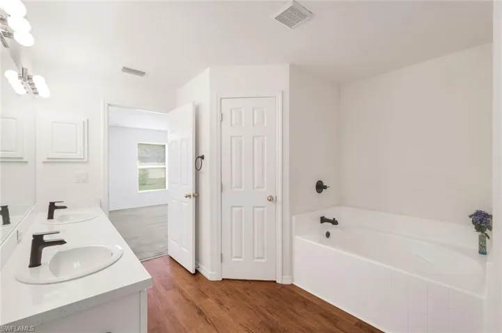Full bathroom featuring double vanity, dark wood-style flooring, and a garden tub