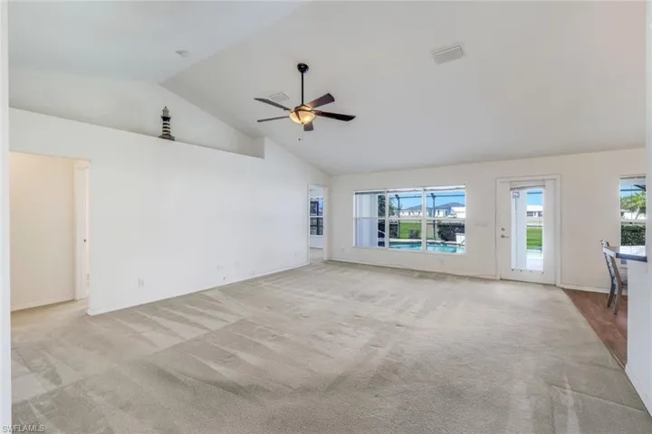 Unfurnished living room featuring a ceiling fan, light colored carpet, and a high ceiling