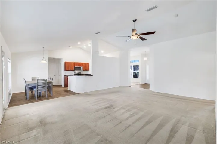 Unfurnished living room with a ceiling fan, lofted ceiling, and light carpet