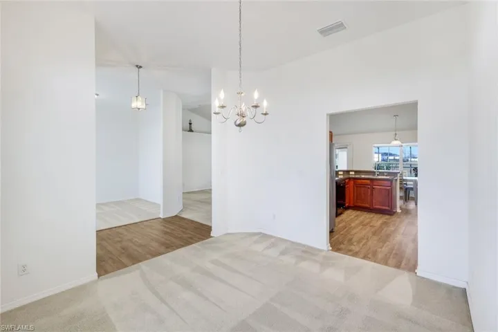 Unfurnished dining area with vaulted ceiling, light colored carpet, a chandelier, and light wood-style flooring