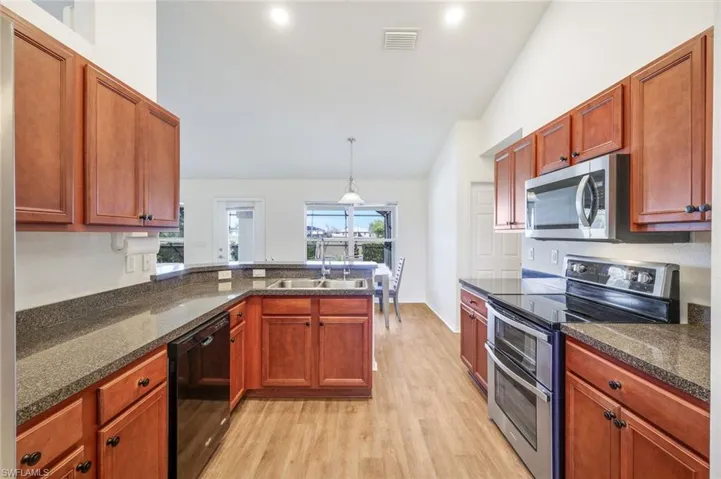 Kitchen with stainless steel appliances, lofted ceiling, a peninsula, light wood-type flooring, and decorative light fixtures