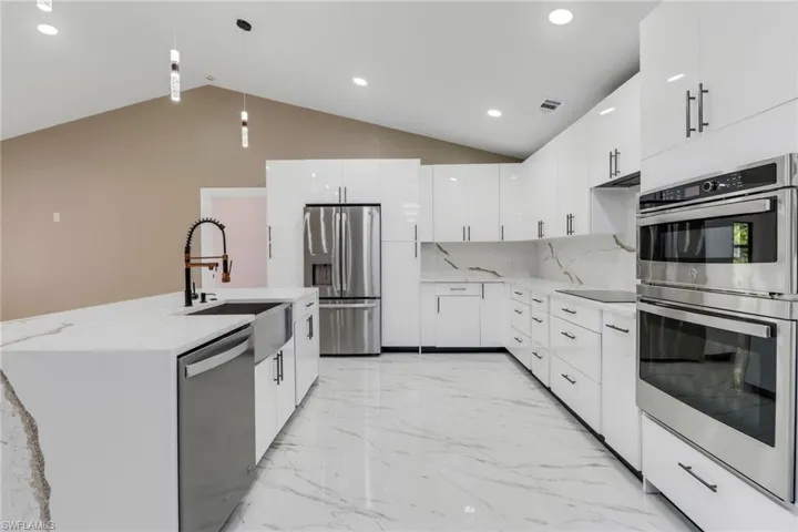 Kitchen featuring appliances with stainless steel finishes, modern cabinets, lofted ceiling, light marble finish flooring, and white cabinets