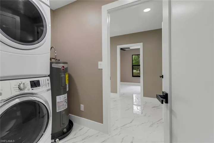 Washroom with stacked washing machine and dryer, electric water heater, and light marble finish floors