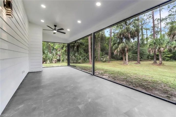 Unfurnished sunroom with ceiling fan and view of wooded area