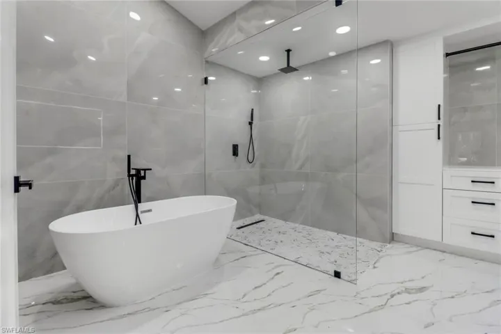 Bathroom featuring marble tiled floors, tile walls, a walk in shower, and a freestanding bath
