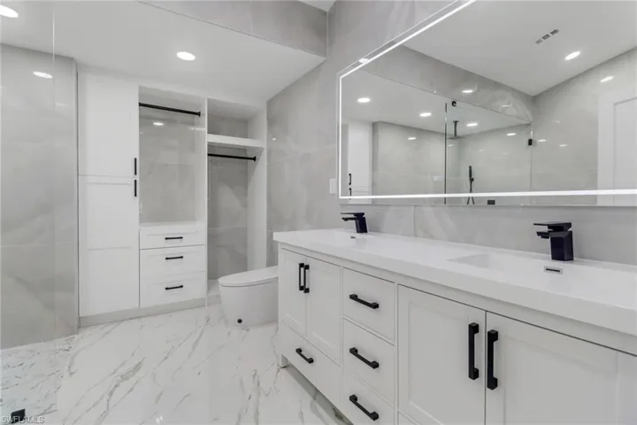 Bathroom featuring double vanity, marble tiled floors, tile walls, a walk in shower, and recessed lighting