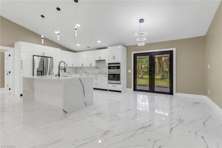 Kitchen featuring stainless steel appliances, light marble finish flooring, white cabinetry, french doors, and vaulted ceiling