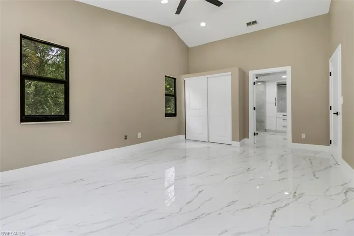 Unfurnished bedroom with high vaulted ceiling, recessed lighting, light marble finish flooring, a closet, and connected bathroom