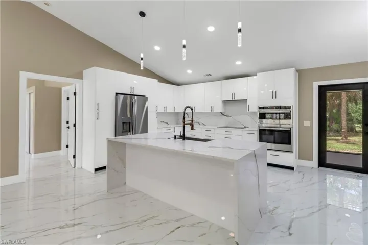 Kitchen with appliances with stainless steel finishes, light marble finish floors, white cabinets, light stone countertops, and lofted ceiling