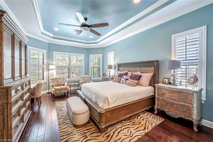 Bedroom with a tray ceiling, multiple windows, hardwood / wood-style floors, recessed lighting, and ornamental molding