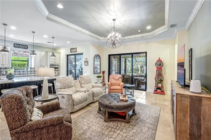 Living area with stone tile flooring, a raised ceiling, recessed lighting, a chandelier, and ornamental molding