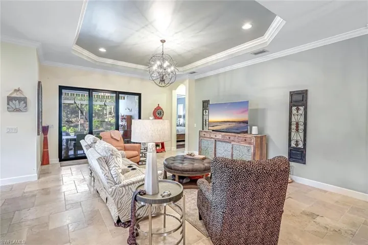 Living area featuring stone tile flooring, a tray ceiling, arched walkways, a chandelier, and recessed lighting