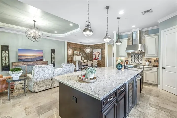 Kitchen with wall chimney range hood, stone tile flooring, a chandelier, open floor plan, and recessed lighting