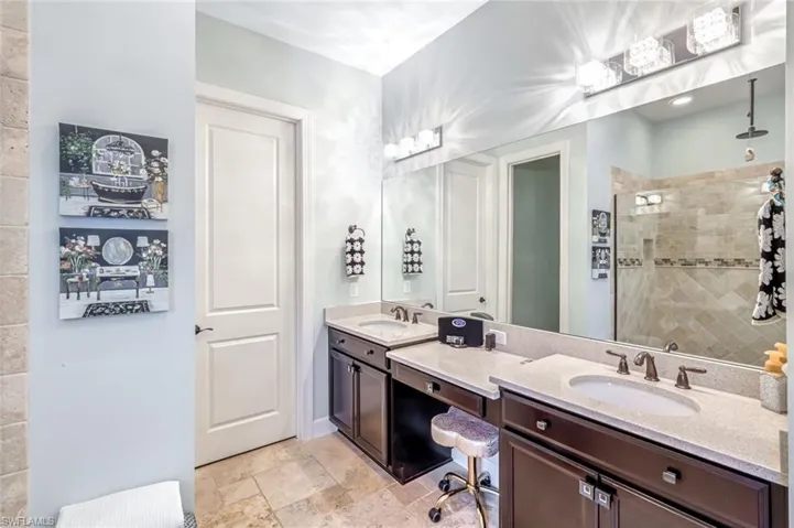Full bathroom with double vanity, a tile shower, and stone finish flooring