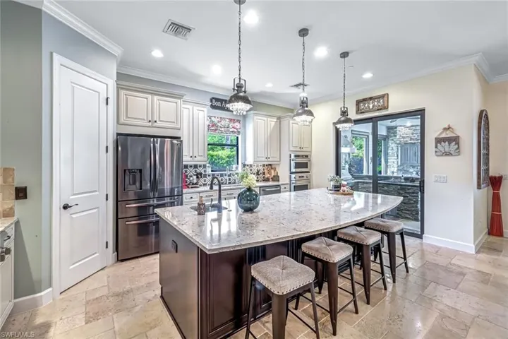 Kitchen featuring stainless steel appliances, stone tile floors, light stone counters, tasteful backsplash, and an island with sink