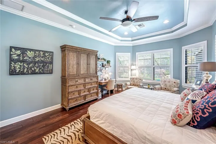 Bedroom with a tray ceiling, dark wood-style floors, ornamental molding, a ceiling fan, and recessed lighting