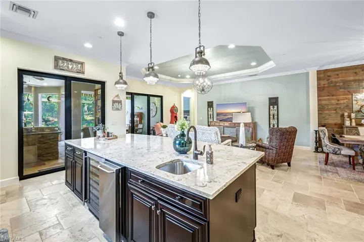 Kitchen featuring stone tile floors, ornamental molding, recessed lighting, open floor plan, and a kitchen island with sink