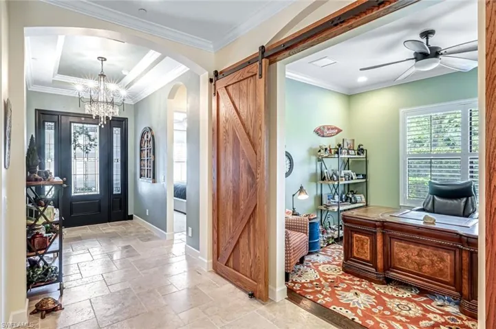 Entrance foyer with arched walkways, a barn door, a chandelier, stone tile floors, and a ceiling fan
