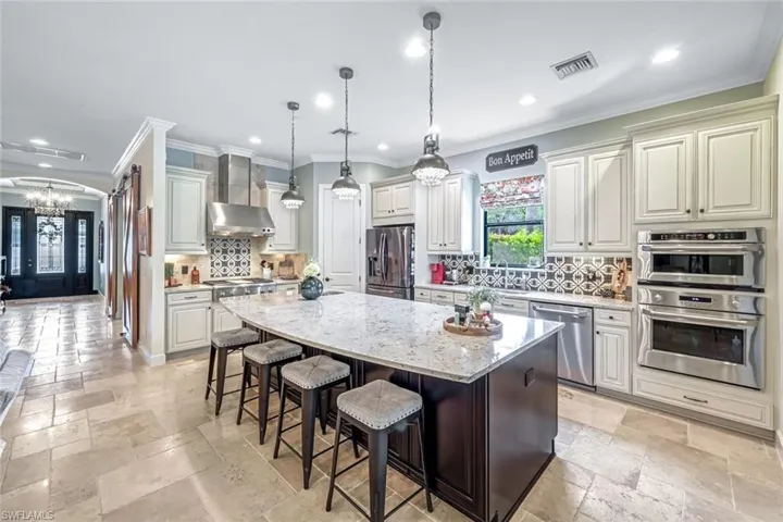 Kitchen featuring stainless steel appliances, a chandelier, recessed lighting, wall chimney range hood, and a center island