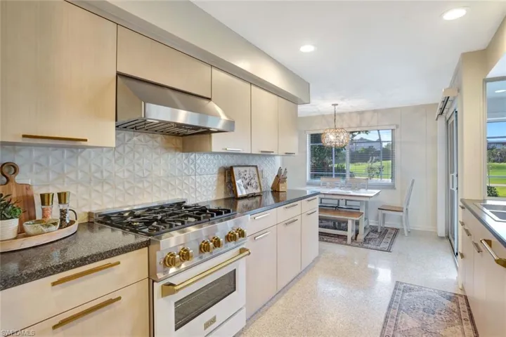 Kitchen featuring decorative backsplash, wall chimney exhaust hood, high end stainless steel range oven, an inviting chandelier, and hanging light fixtures