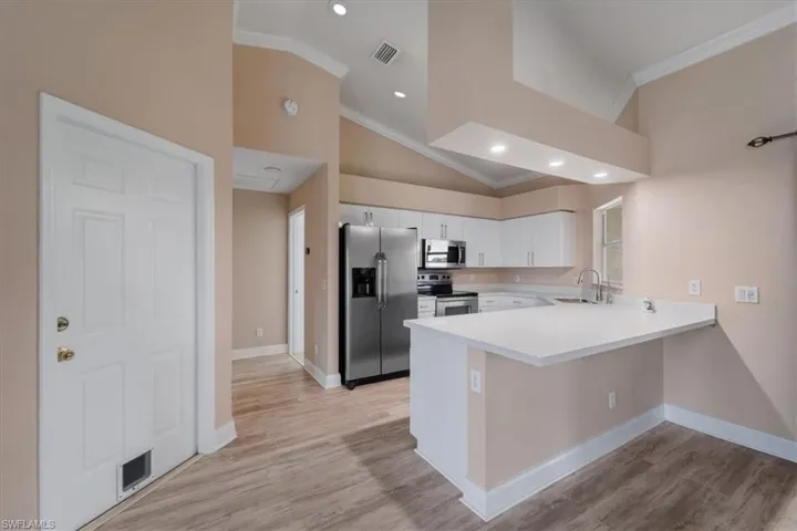 Kitchen with light countertops, appliances with stainless steel finishes, ornamental molding, white cabinetry, and a peninsula