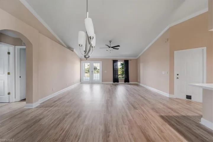 Unfurnished living room featuring crown molding, light wood-style floors, arched walkways, ceiling fan, and french doors