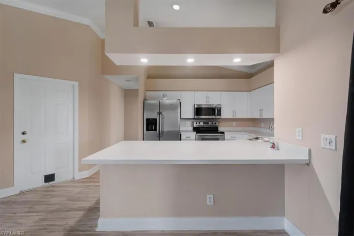 Kitchen featuring appliances with stainless steel finishes, a peninsula, white cabinets, crown molding, and recessed lighting