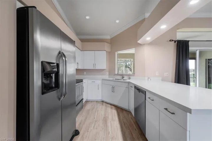Kitchen with stainless steel appliances, ornamental molding, light countertops, white cabinets, and light wood finished floors