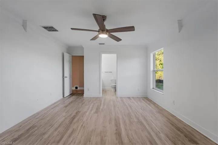Unfurnished bedroom featuring crown molding, light wood-style flooring, a ceiling fan, and ensuite bathroom
