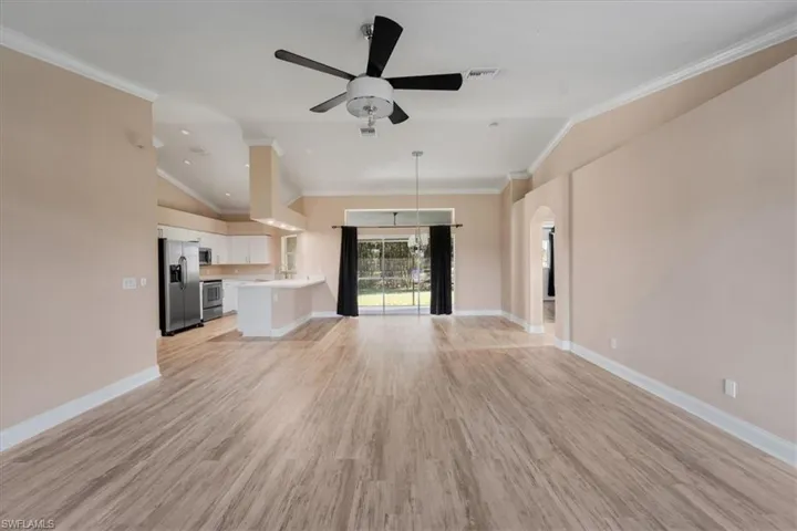Unfurnished living room with crown molding, light wood finished floors, vaulted ceiling, ceiling fan, and arched walkways
