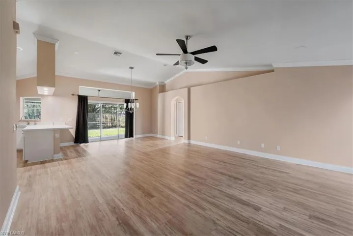 Unfurnished living room featuring ornamental molding, light wood-style floors, arched walkways, a ceiling fan, and lofted ceiling