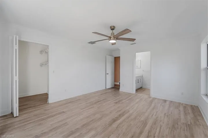 Unfurnished bedroom with a spacious closet, light wood-style floors, ceiling fan, and ensuite bathroom