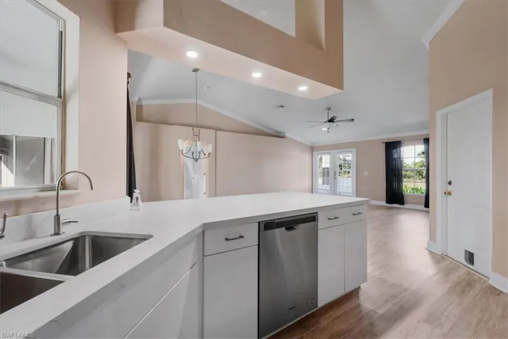 Kitchen featuring ceiling fan, ornamental molding, stainless steel dishwasher, white cabinetry, and a chandelier