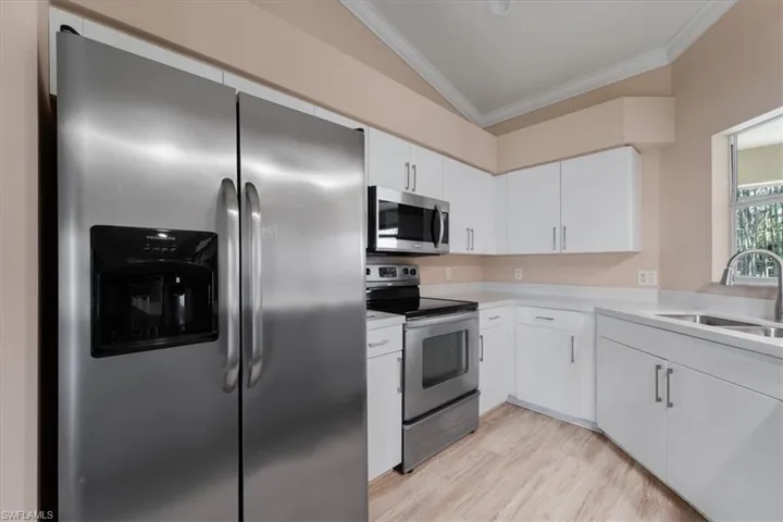 Kitchen with stainless steel appliances, crown molding, light countertops, light wood-type flooring, and white cabinetry