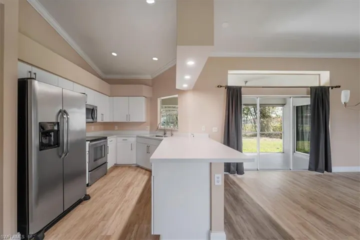 Kitchen with crown molding, stainless steel appliances, light countertops, white cabinetry, and recessed lighting