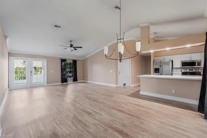 Unfurnished living room with a chandelier, crown molding, light wood-type flooring, lofted ceiling, and a ceiling fan
