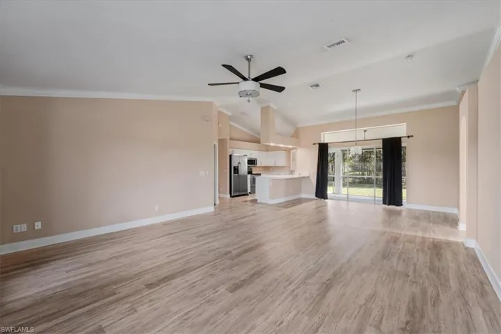 Unfurnished living room with crown molding, light wood-style floors, ceiling fan, and vaulted ceiling