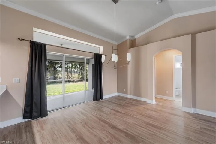 Unfurnished dining area featuring crown molding, vaulted ceiling, a chandelier, light wood-style flooring, and arched walkways