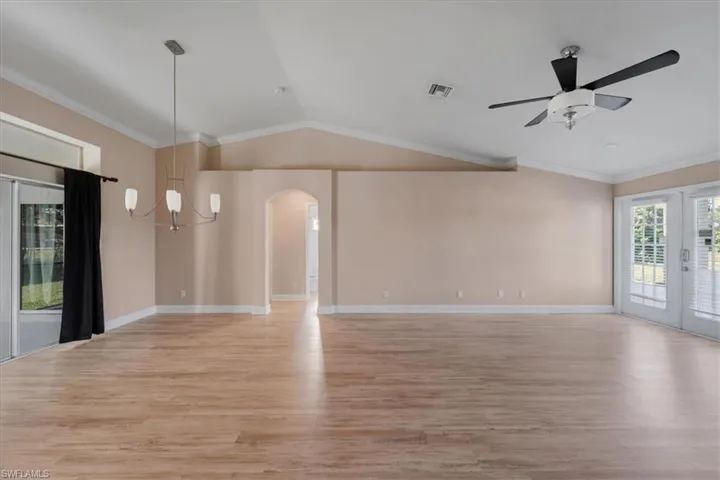 Unfurnished living room with crown molding, light wood-type flooring, a chandelier, lofted ceiling, and ceiling fan