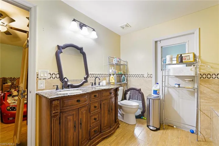Bathroom featuring tile walls, wood finished floors, a wainscoted wall, and double vanity