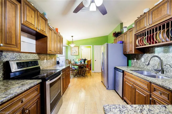 Kitchen featuring stainless steel appliances, backsplash, lofted ceiling, a ceiling fan, and light wood-style floors