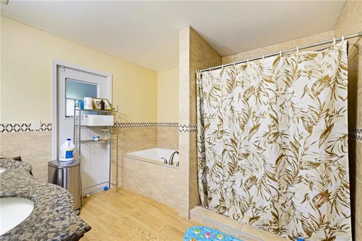 Bathroom with wood finished floors, curtained shower, a bath, vanity, and tile walls